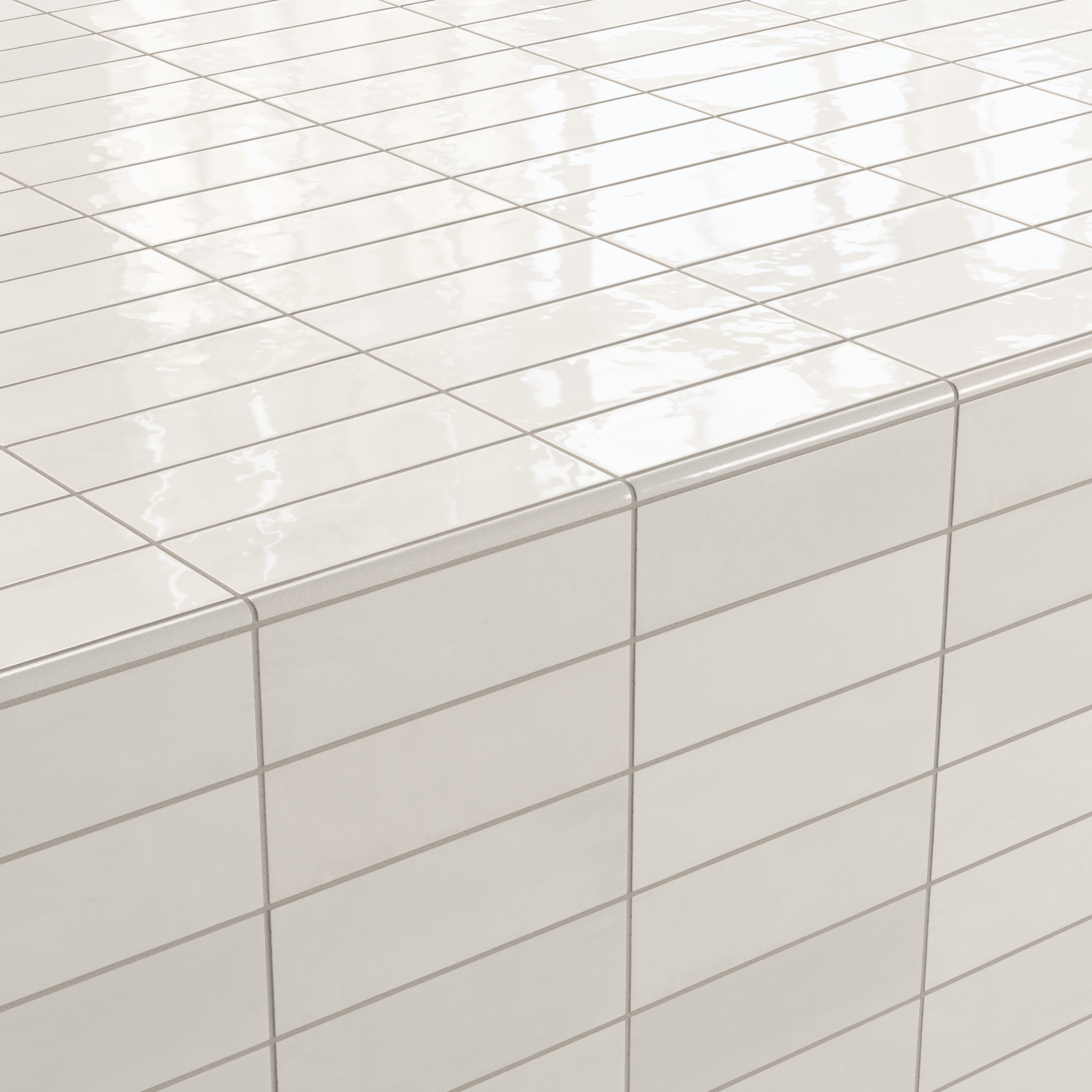 Corner detail of glossy subway tiles in shifting white tones, finished with a rounded tile edge trim for a smooth and seamless transition