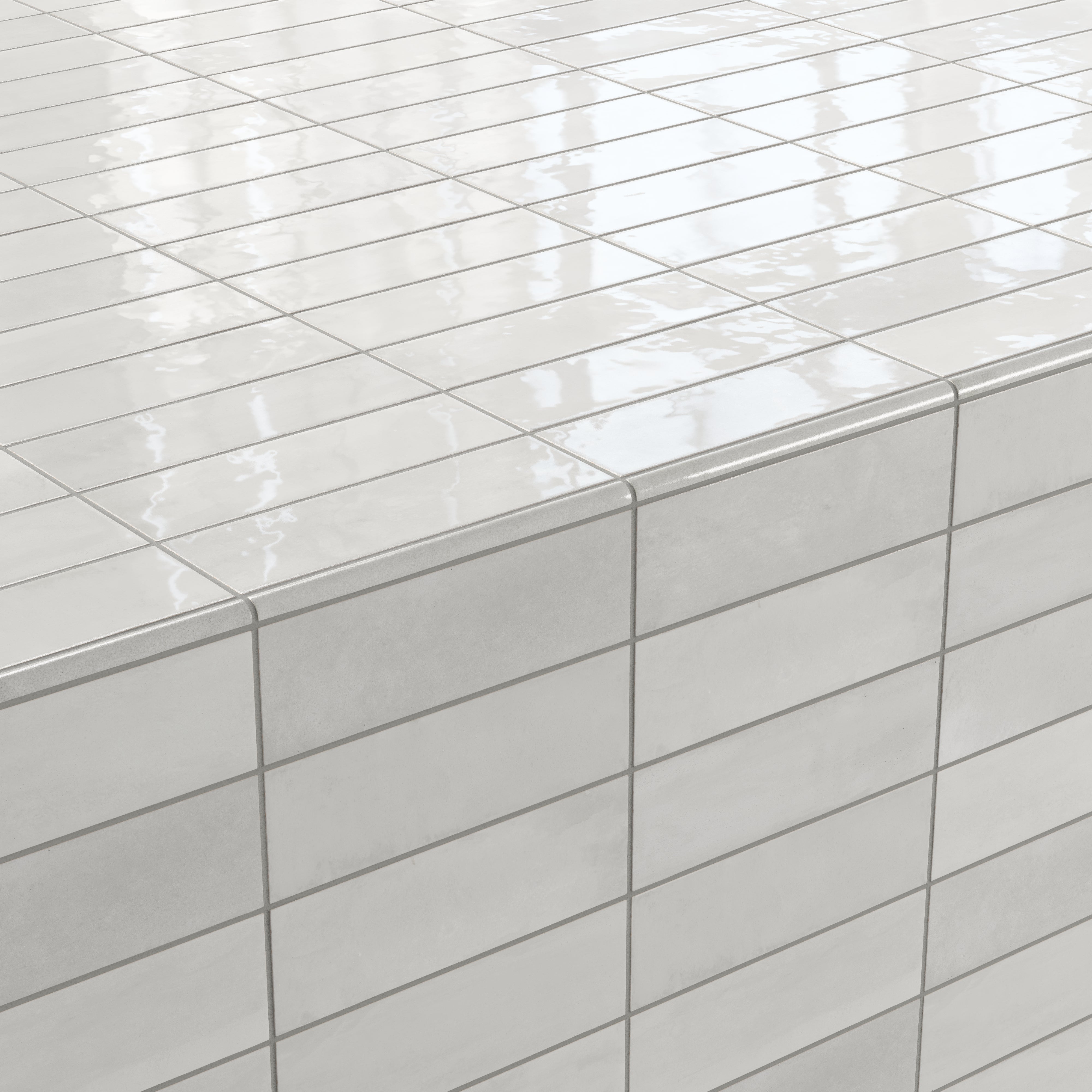Corner detail of glossy ceramic subway tiles in shifting light gray tones, finished with a rounded tile edge trim for a seamless, polished transition