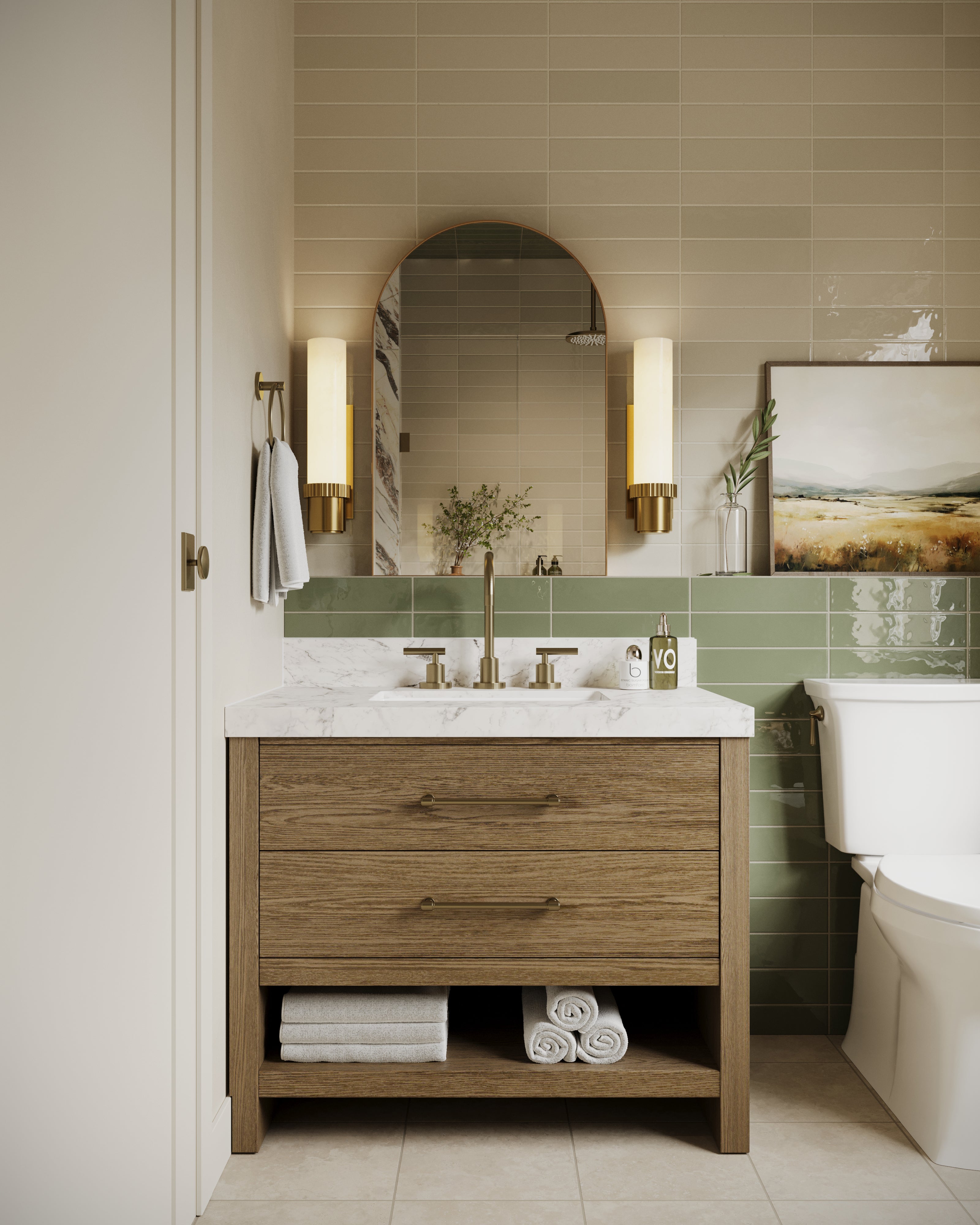 Brass bathroom wall sconces with tall cylindrical diffusers and fluted metal bases flanking an arched mirror above the vanity, casting warm ambient light against beige and green subway tiles in a modern bathroom.