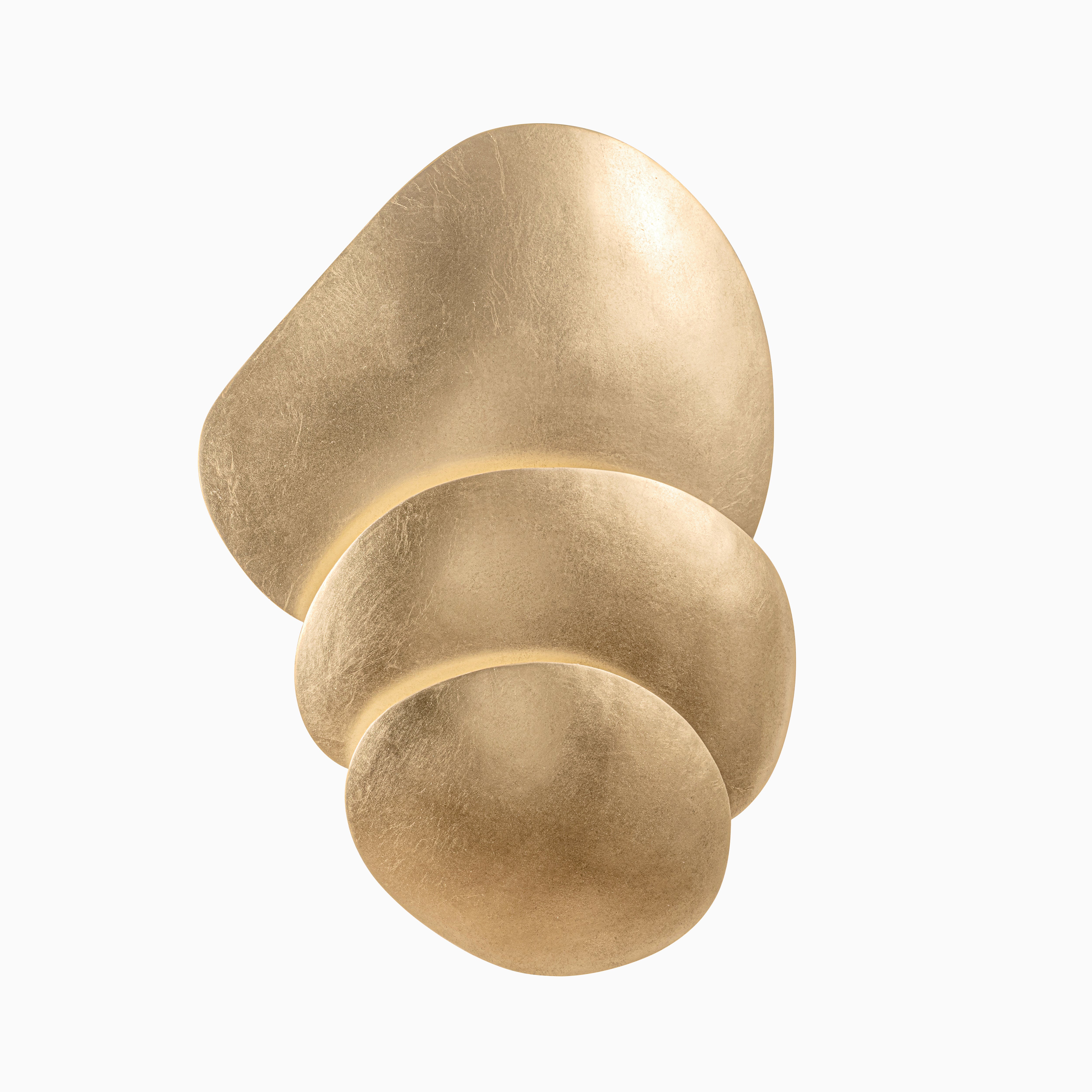 Wall sconce with stacked, organic gold forms resembling river stones, casting soft ambient light with a warm, luminous glow.