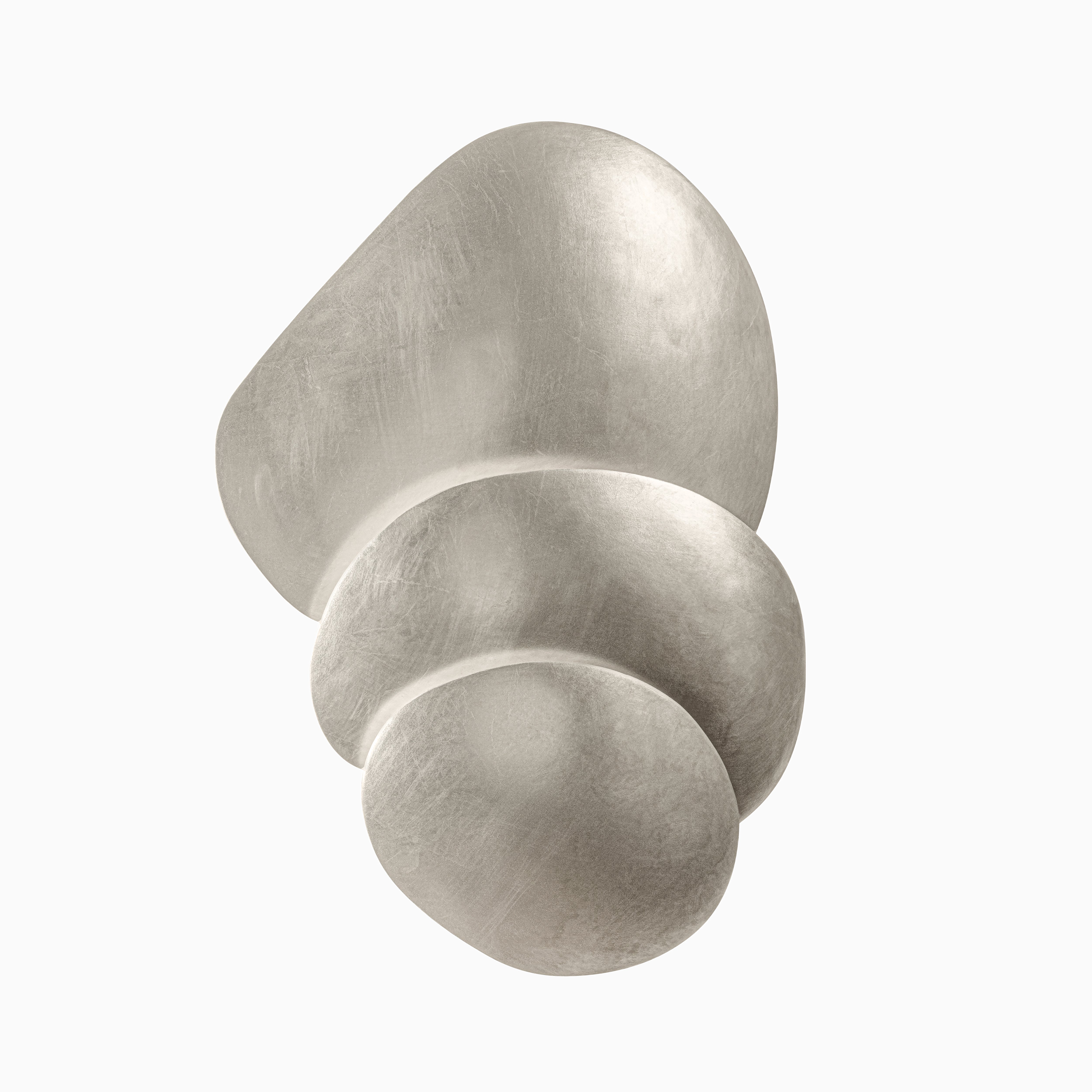 Wall sconce with layered, pebble-inspired metal forms in warm silver, casting soft ambient light with sculptural elegance.
