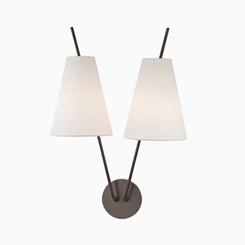 Old bronze wall sconce with round backplate, dual angled arms, and tapered white fabric shades for a sleek modern symmetrical design.