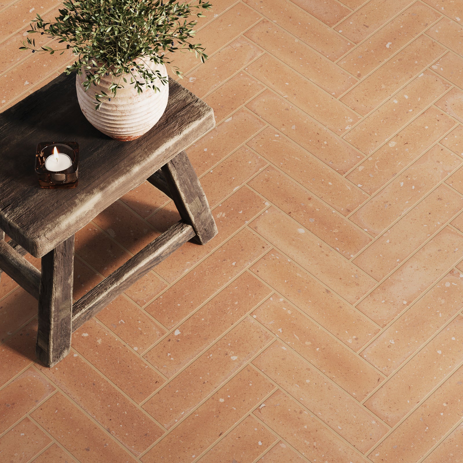 Herringbone-patterned orange subway tiles with soft speckles, paired with a rustic wooden stool and a decorative plant, adding warmth and charm.