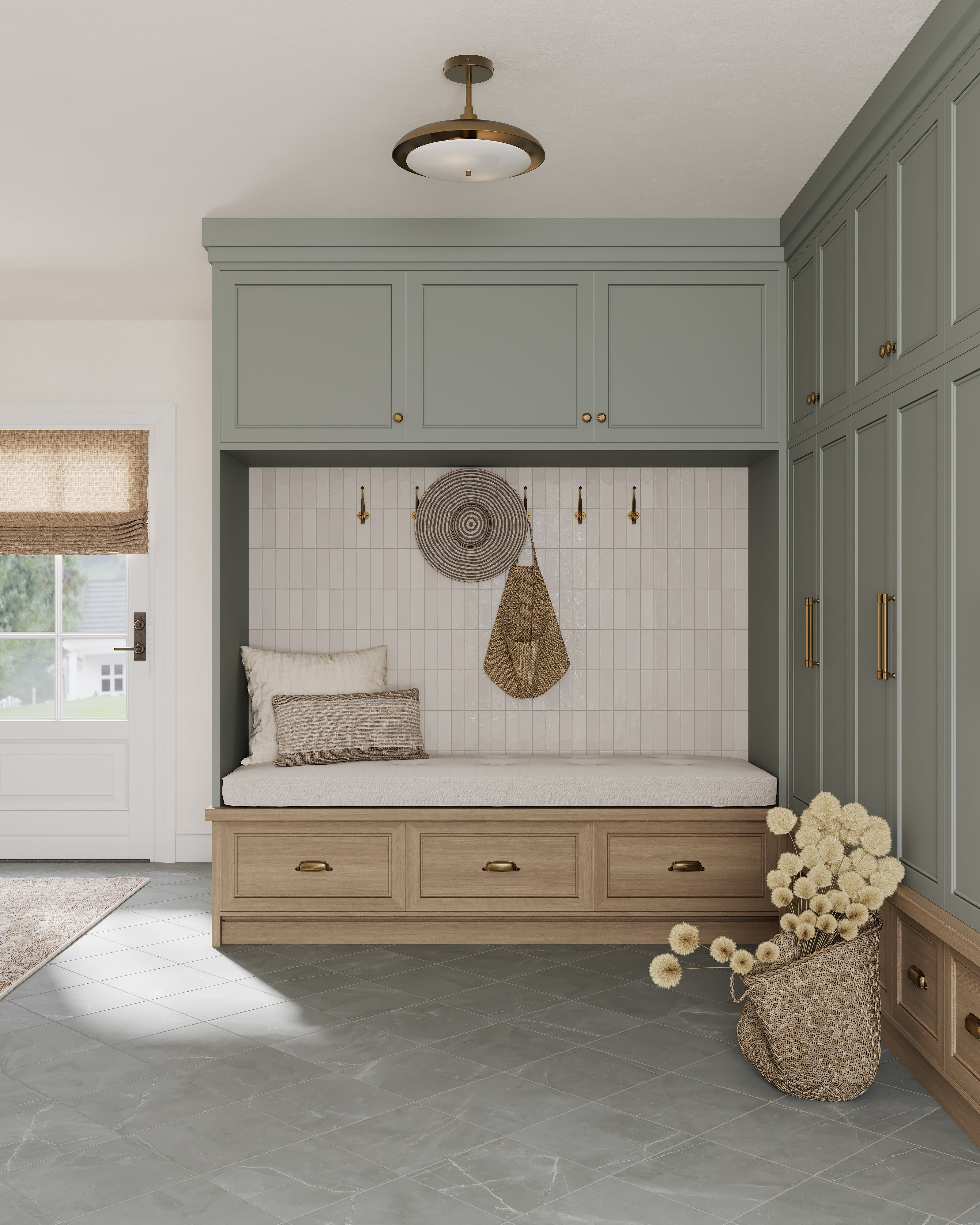 Mudroom with glossy white subway tile wall, built-in bench with drawers and cushions, sage green cabinetry, woven circular wall decor, straw bag on gold hooks, and gray tiled floor with a woven basket of flowers.