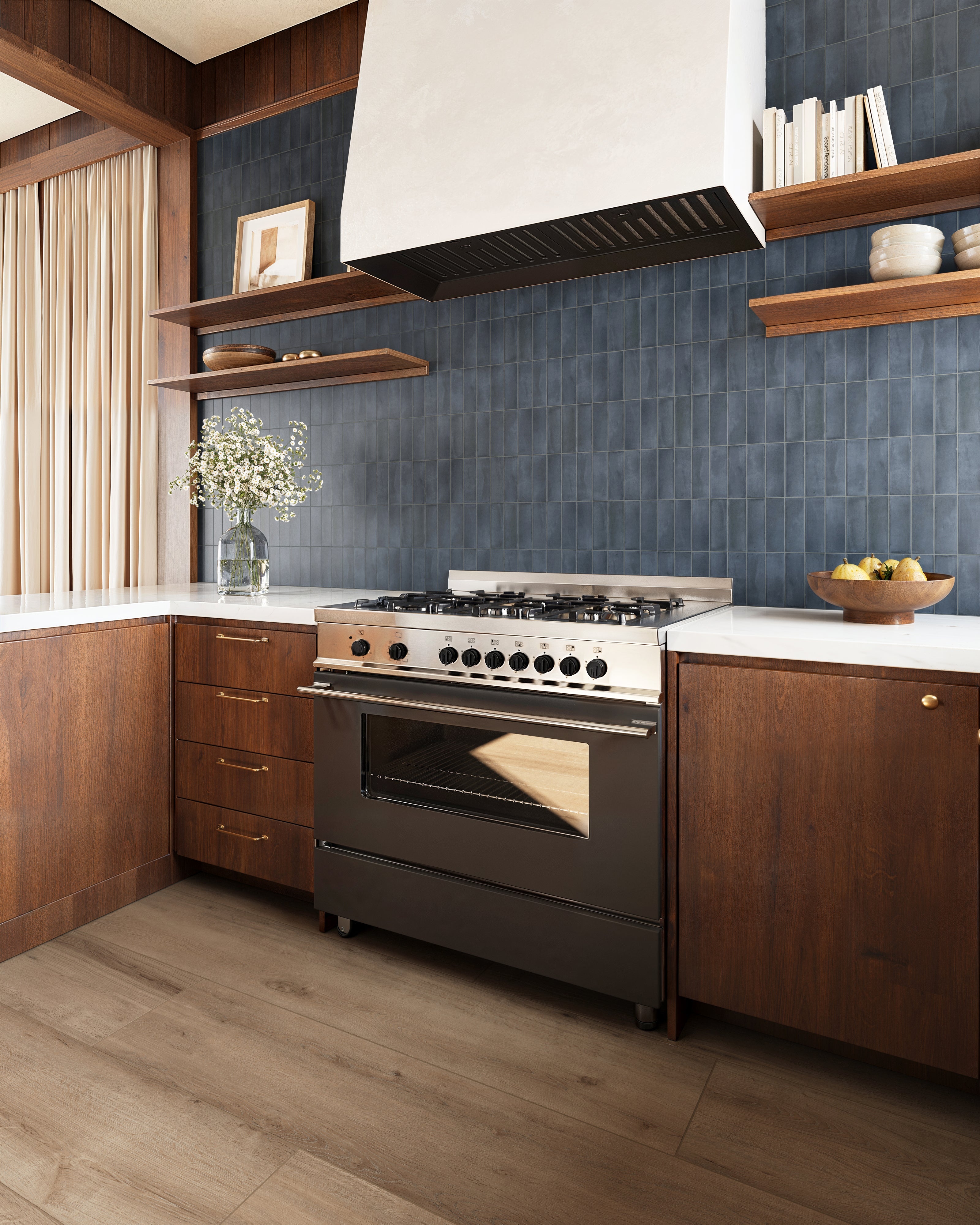 Sophisticated kitchen backsplash featuring Natasha 2x6 matte porcelain tile in Denim with deep navy blue tones, complemented by warm wood cabinetry, white countertops, and sleek stainless steel appliances.