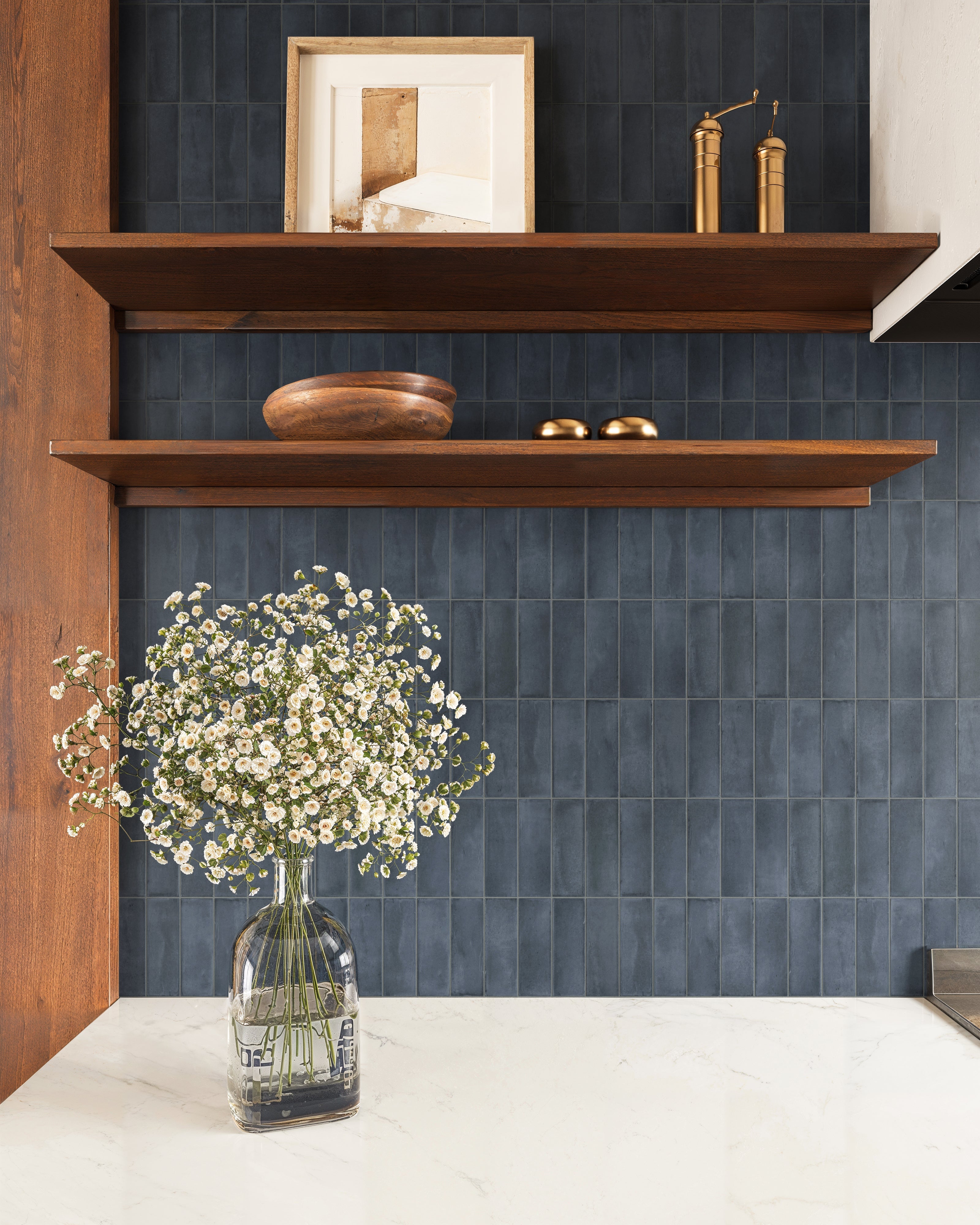 Blue matte tiles create a rich, textured backsplash, complementing warm wood shelves and a marble countertop.