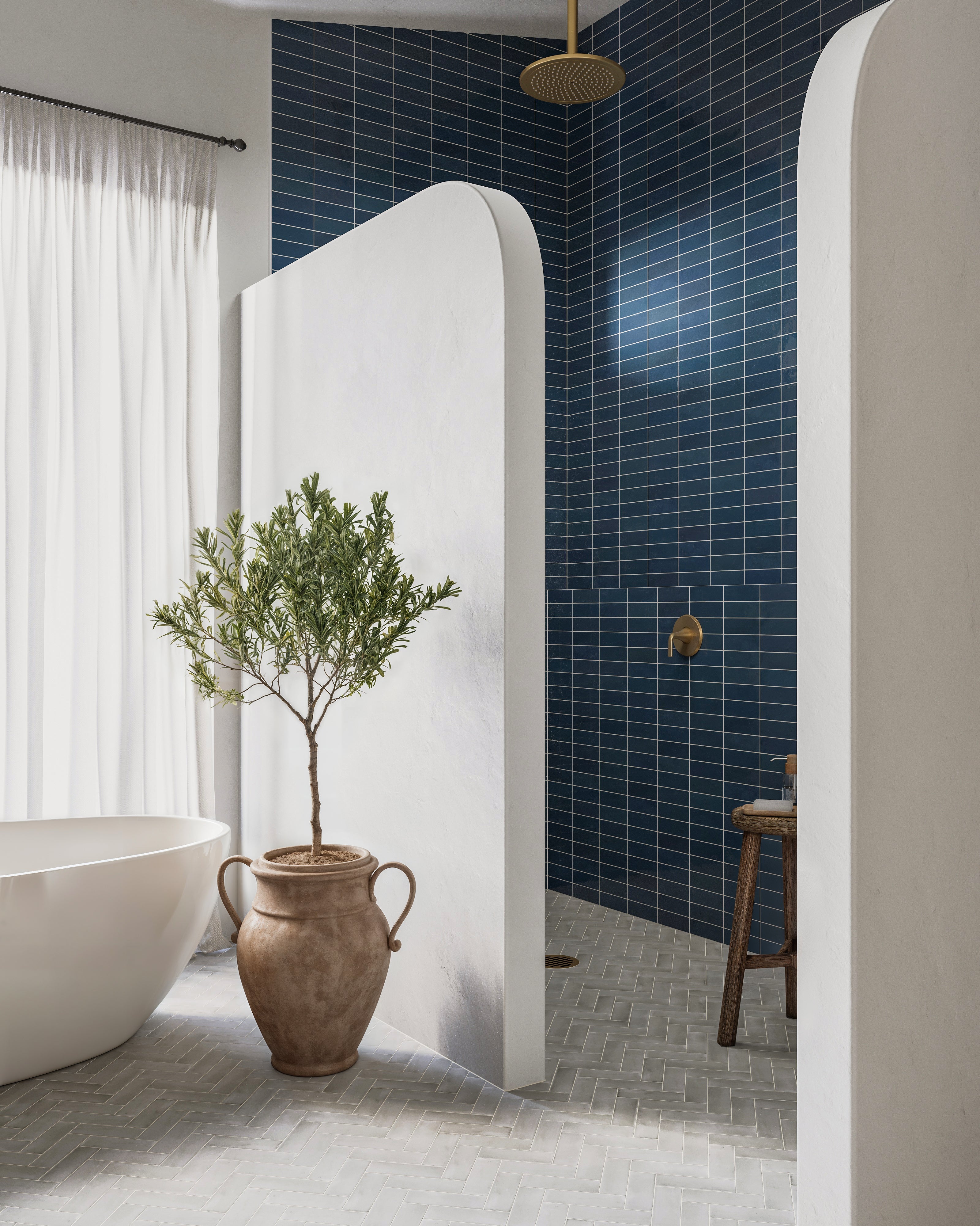 A spa-like bathroom with denim blue glossy subway tiles in the shower, brass fixtures, and light gray herringbone floor tiles extending throughout.