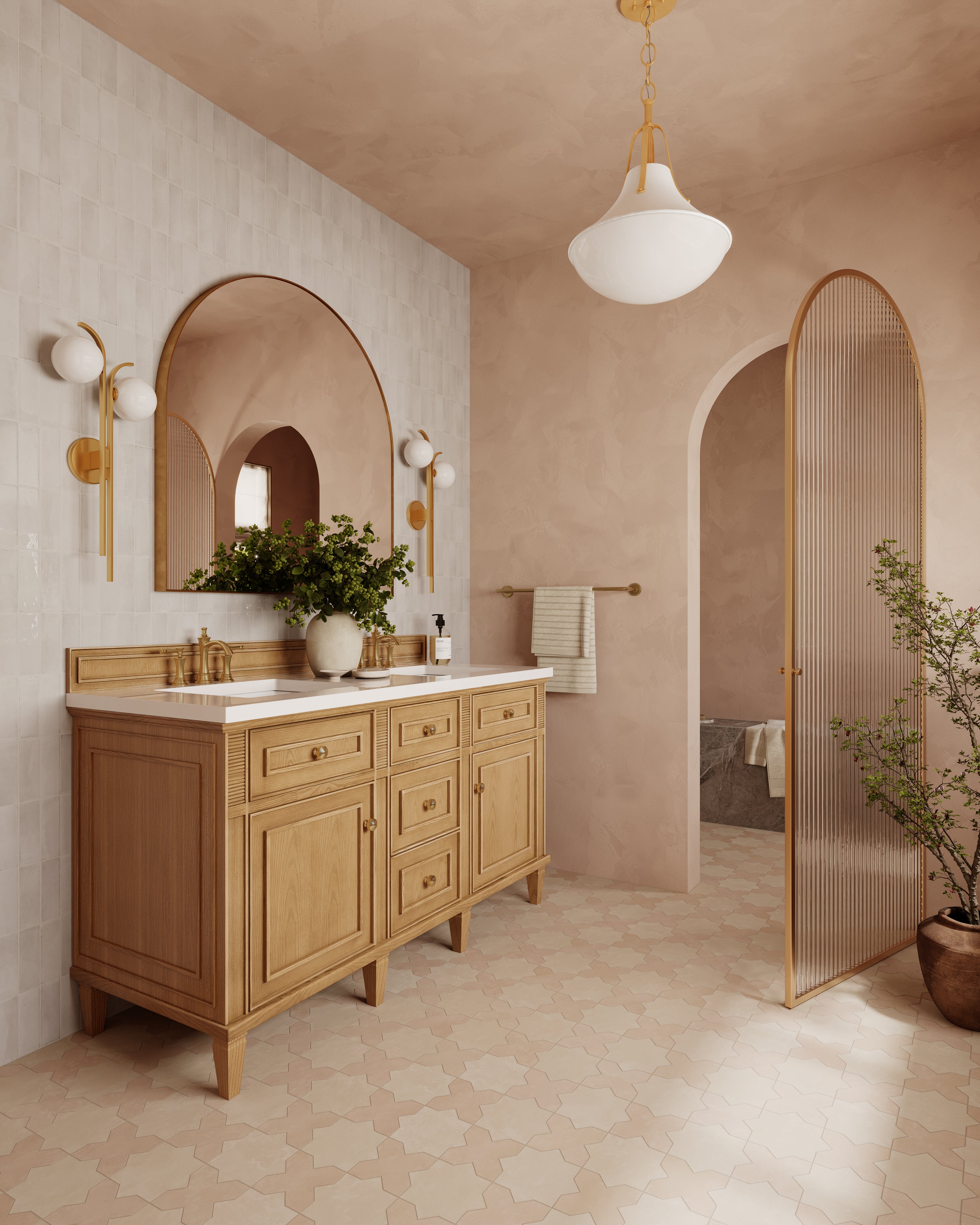Vintage gold leaf pendant light with a sculptural flared shade and smooth white diffuser, illuminating a warm, blush-toned bathroom with arched details, natural wood cabinetry, and patterned tile flooring.
