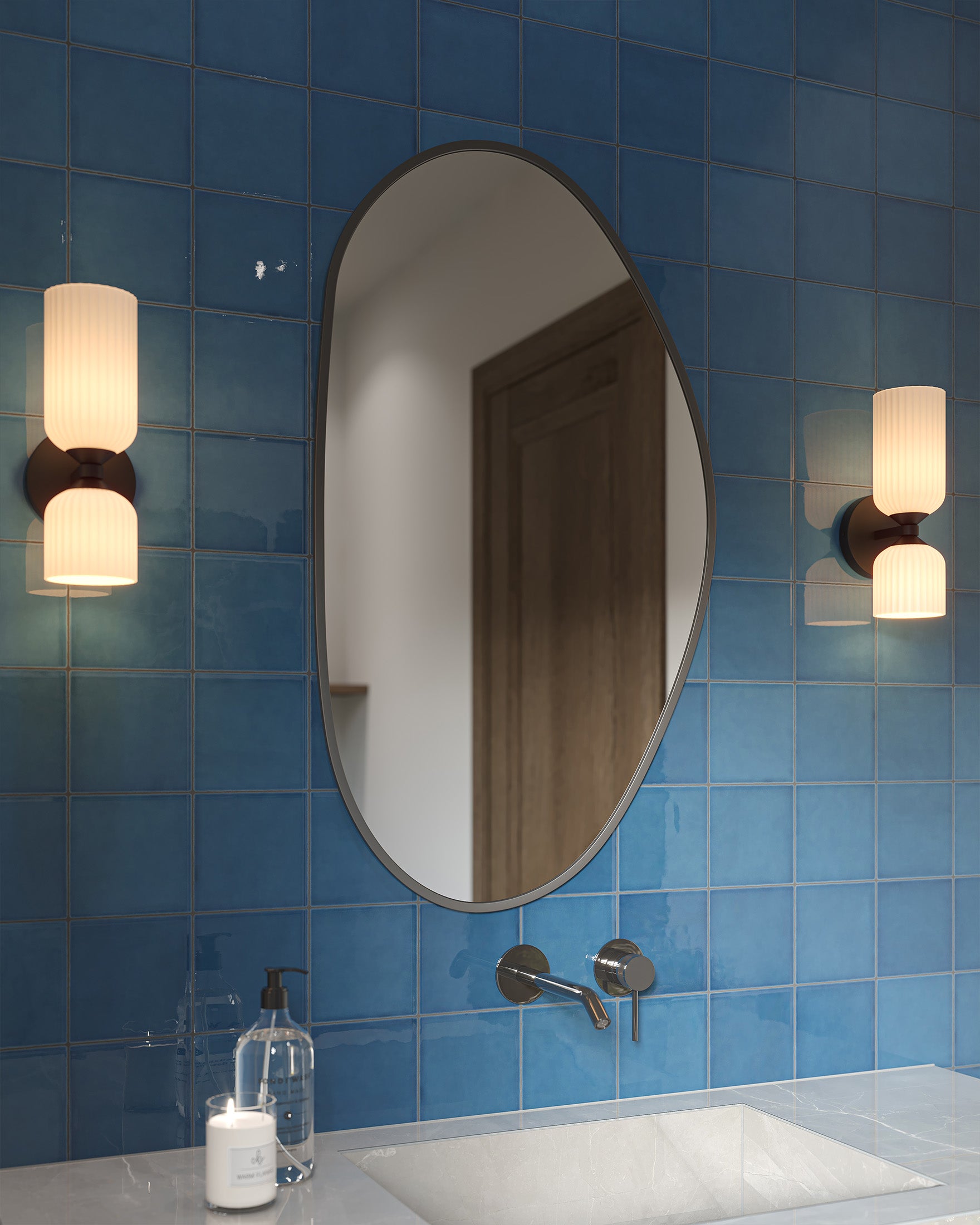 Pair of ribbed glass vanity lights mounted beside an oval mirror on deep blue ceramic tiles, illuminating a clean modern bathroom sink area.