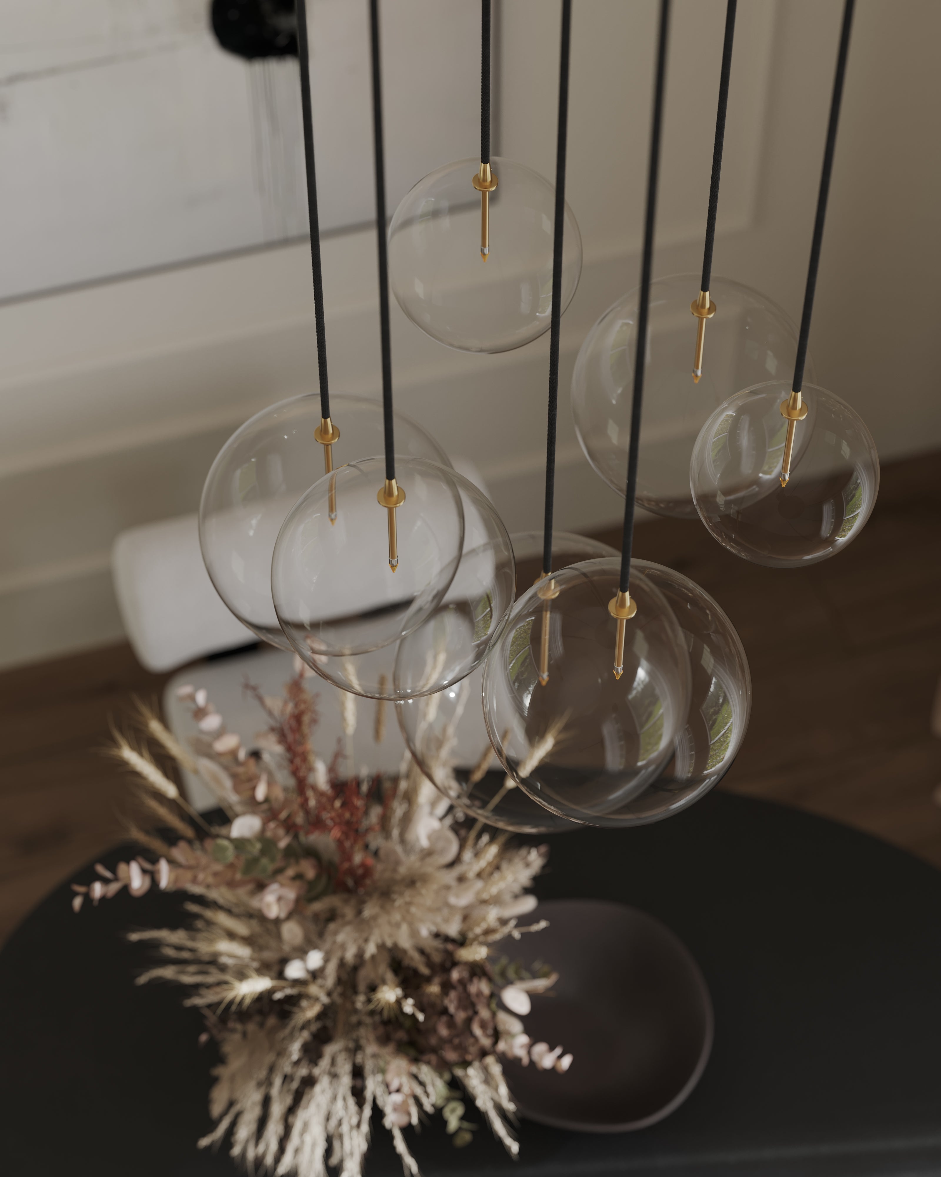 Cluster of clear glass globe pendants with brass details suspended from black cords above a dining table with a dried floral arrangement