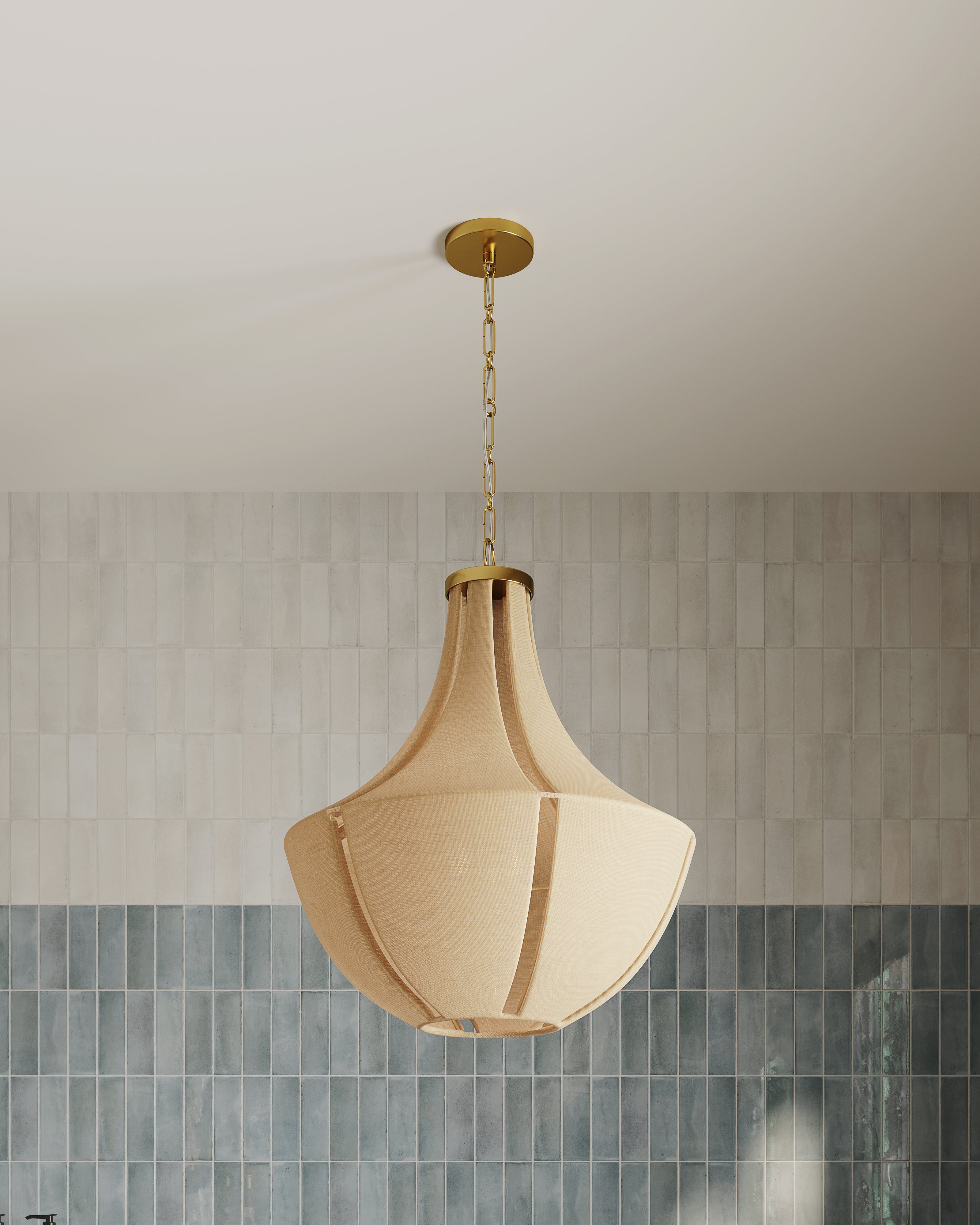 Aged brass pendant light with a sculptural, curved fabric shade suspended from a brass chain, centered against a backdrop of vertically stacked neutral and blue-toned tiles in a modern interior.