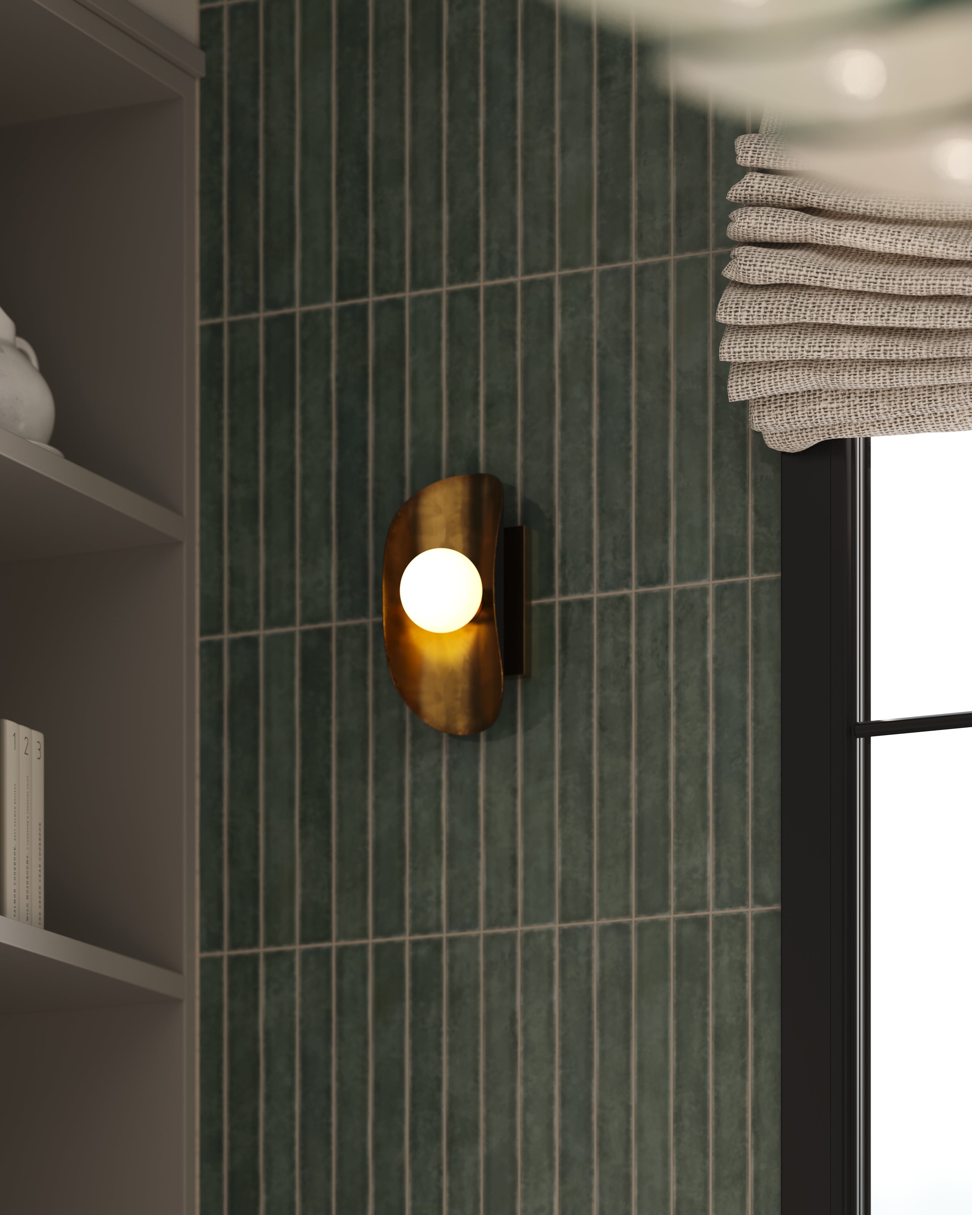 Vintage brass wall sconce with a rounded backplate and glowing globe bulb mounted on a vertical green tile wall beside a window in a modern kitchen
