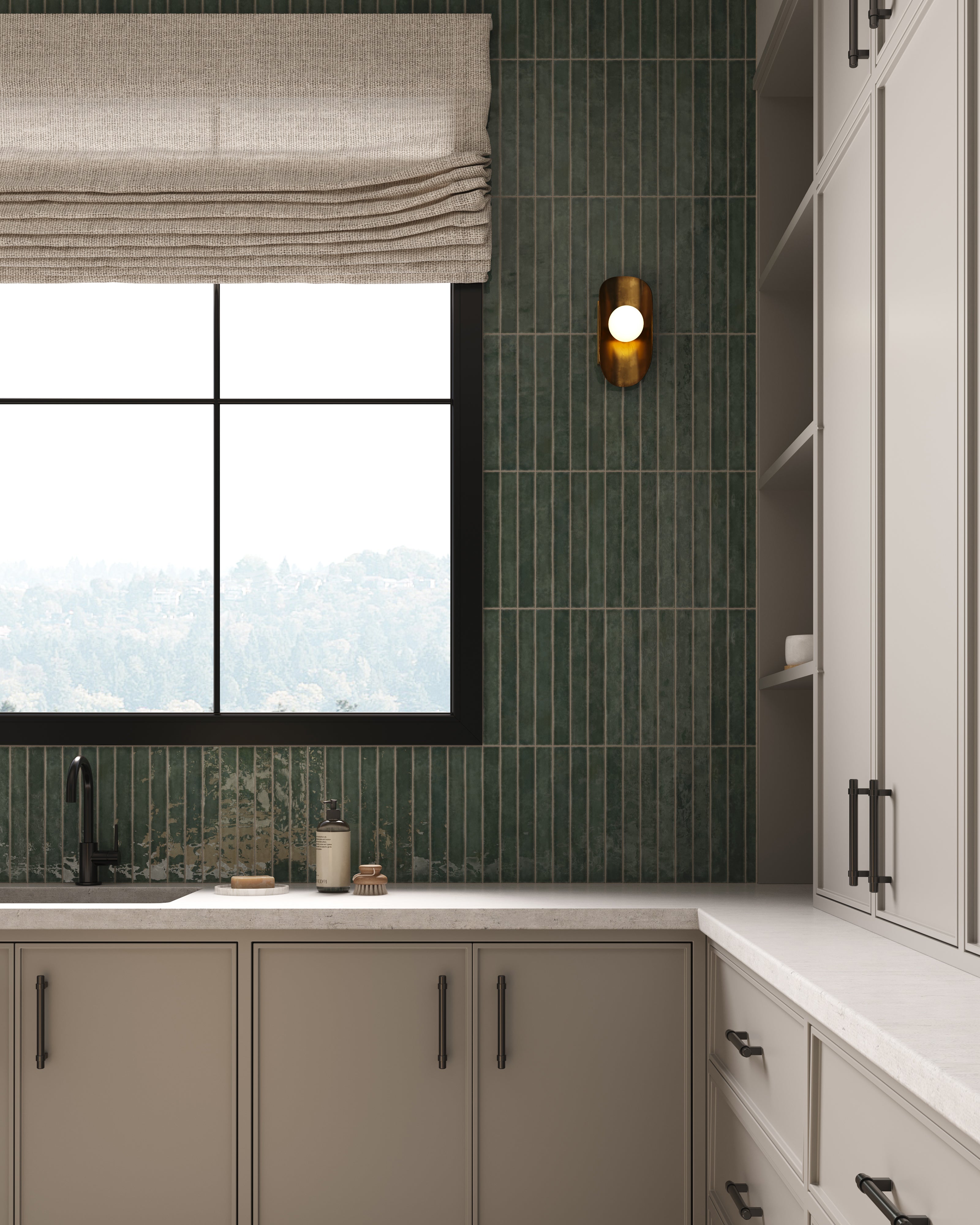 Refined kitchen sink area with vertical green tile backsplash, a brass-accent wall sconce, soft Roman shade, and light cabinetry creating a calm, modern kitchen aesthetic.