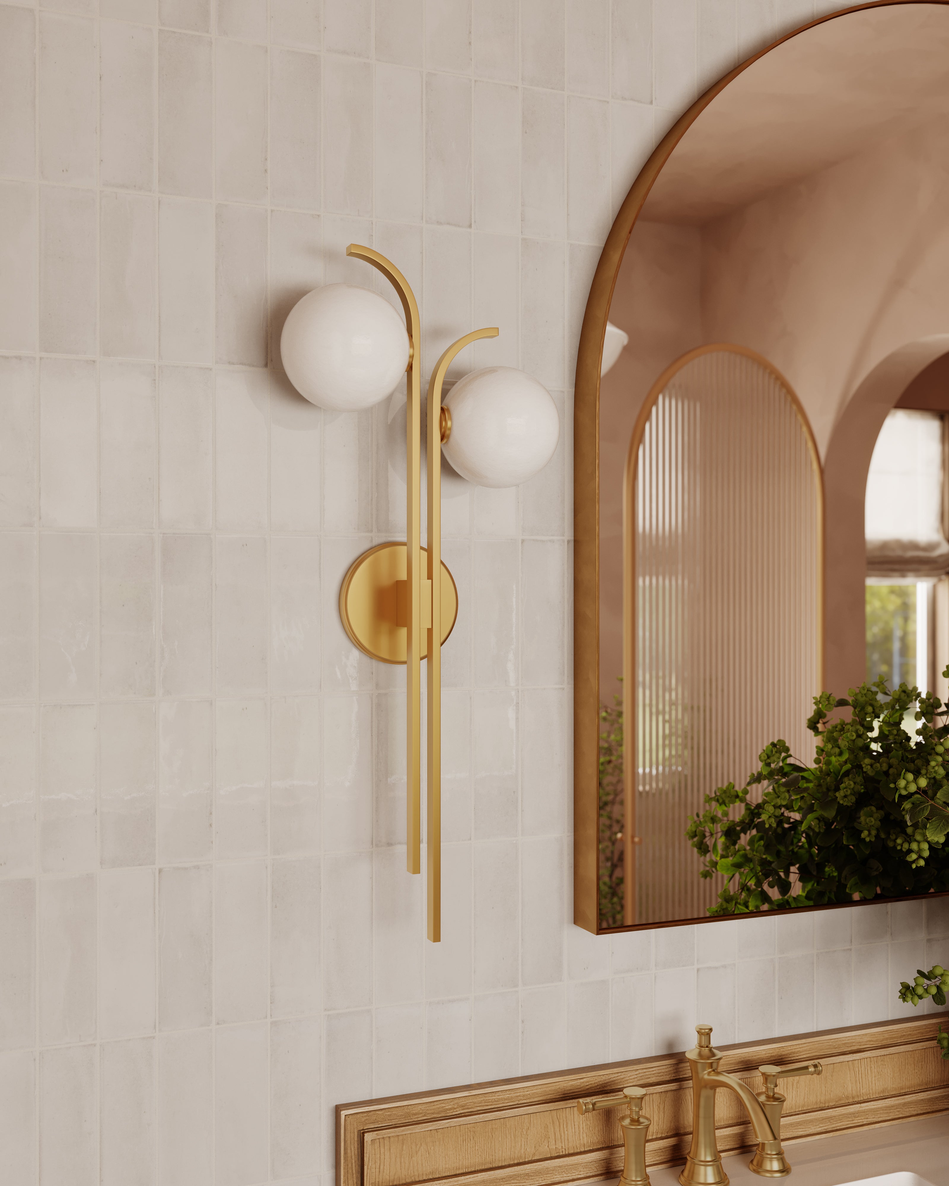 Bathroom with an aged brass wall sconce featuring two frosted glass globes, mounted beside an arched mirror above a brass faucet.