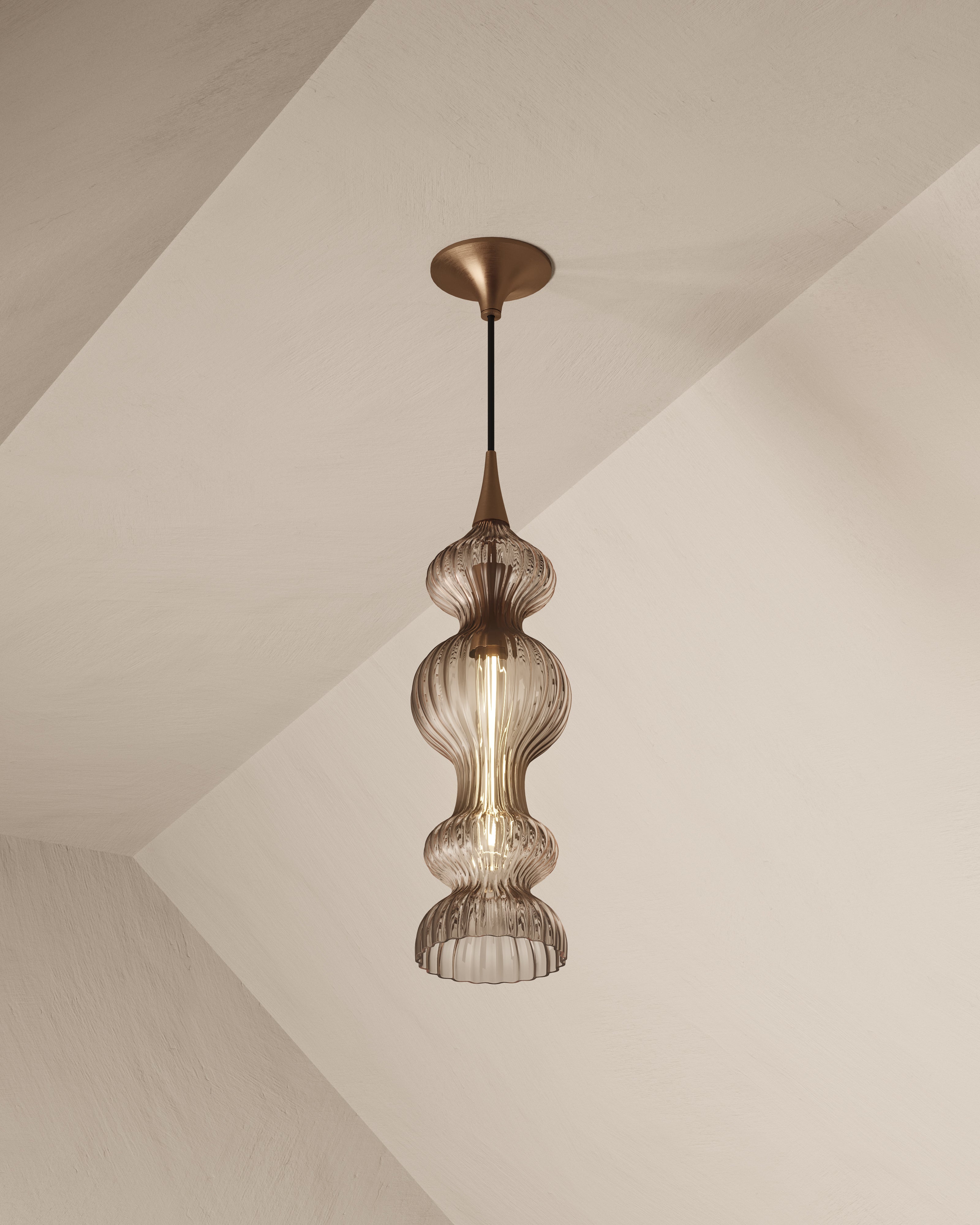 Pendant light with tiered, ribbed bronze glass shade and aged brass detailing, casting a warm, ambient glow in modern interiors.