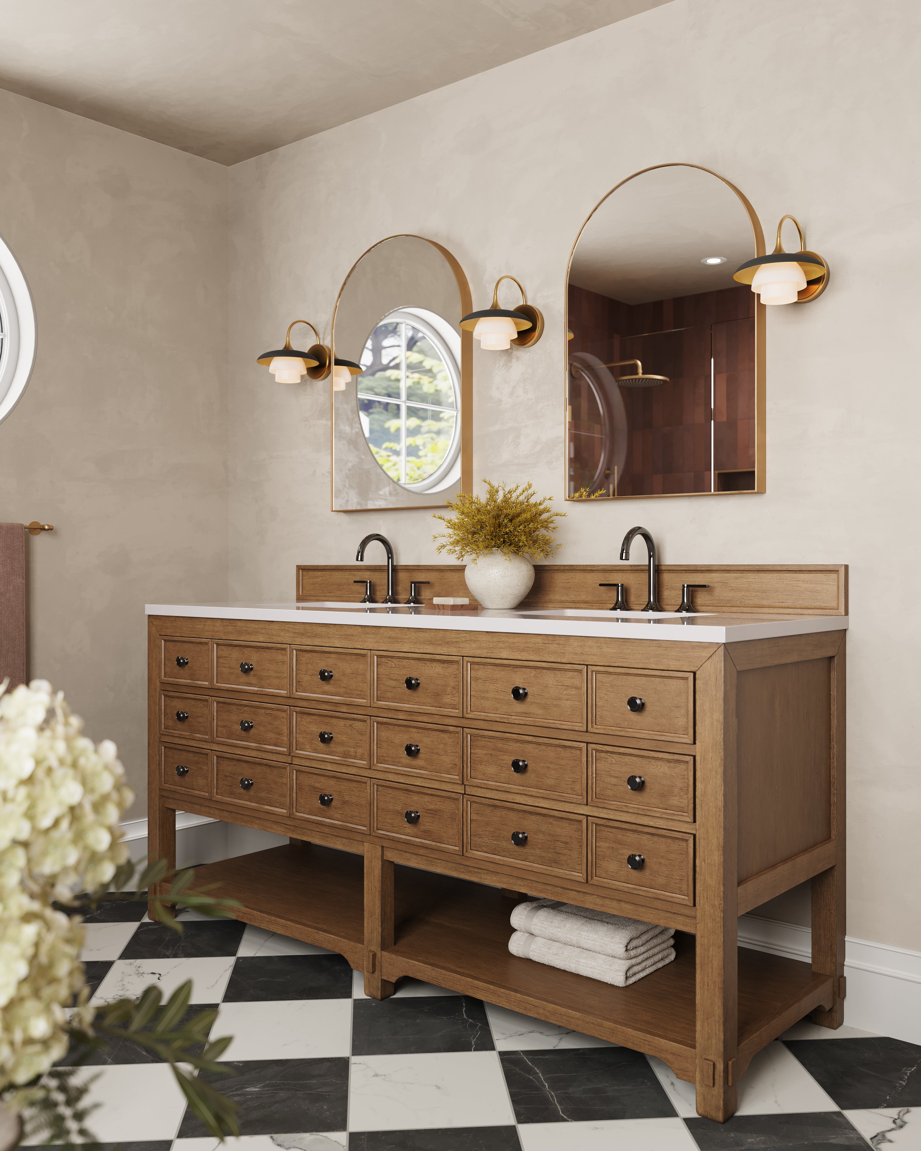 Aged brass bathroom wall sconces with curved metal arms and layered frosted glass shades flanking arched mirrors, providing warm ambient lighting above a double vanity with natural wood cabinetry and black hardware.