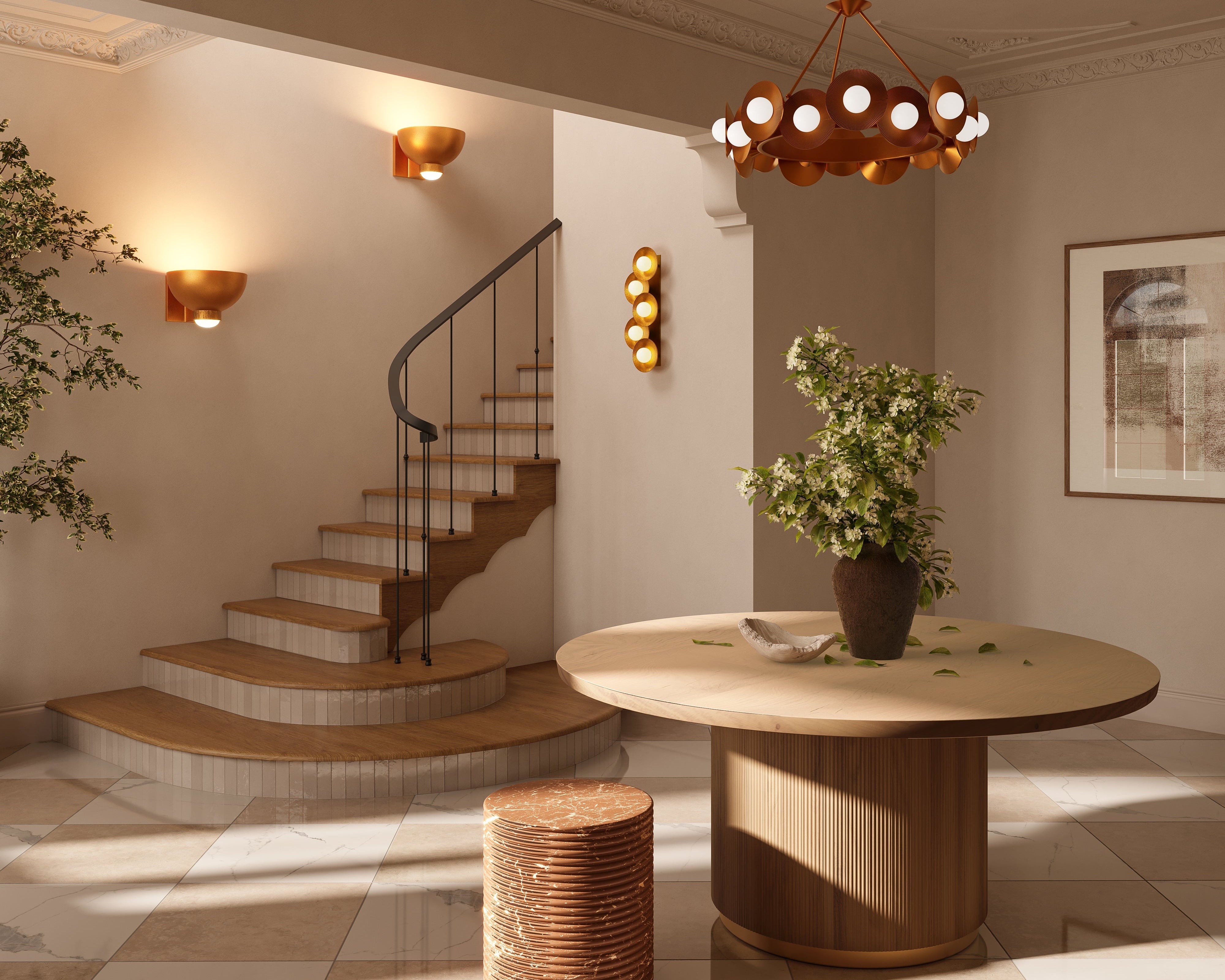 Vintage gold leaf wall sconce with circular disc shades and warm globe bulbs mounted on a neutral entryway wall near the staircase.