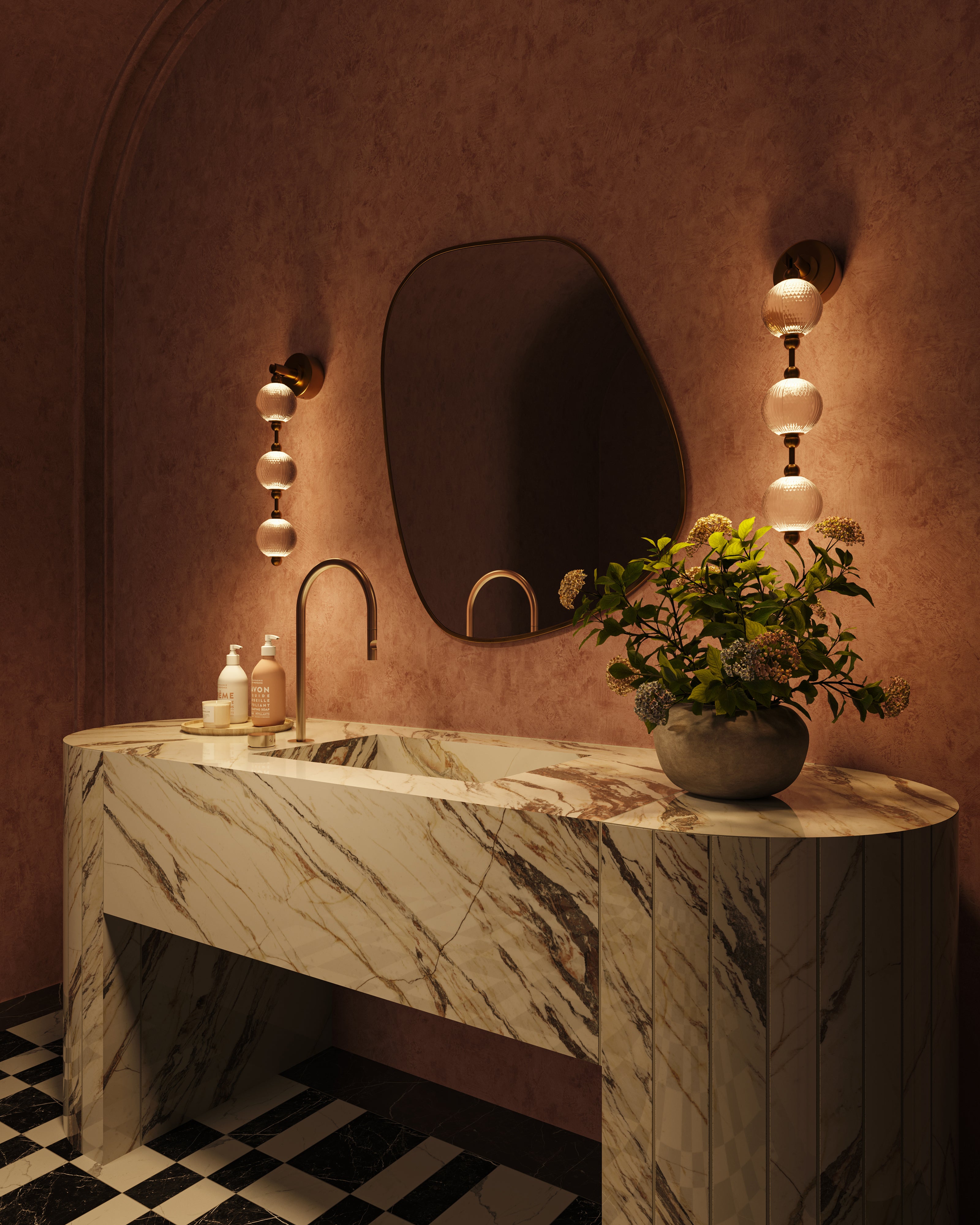 Pair of brushed gold vanity lights with textured glass globe shades mounted beside a sculptural mirror above a marble vanity in a warm bathroom setting.