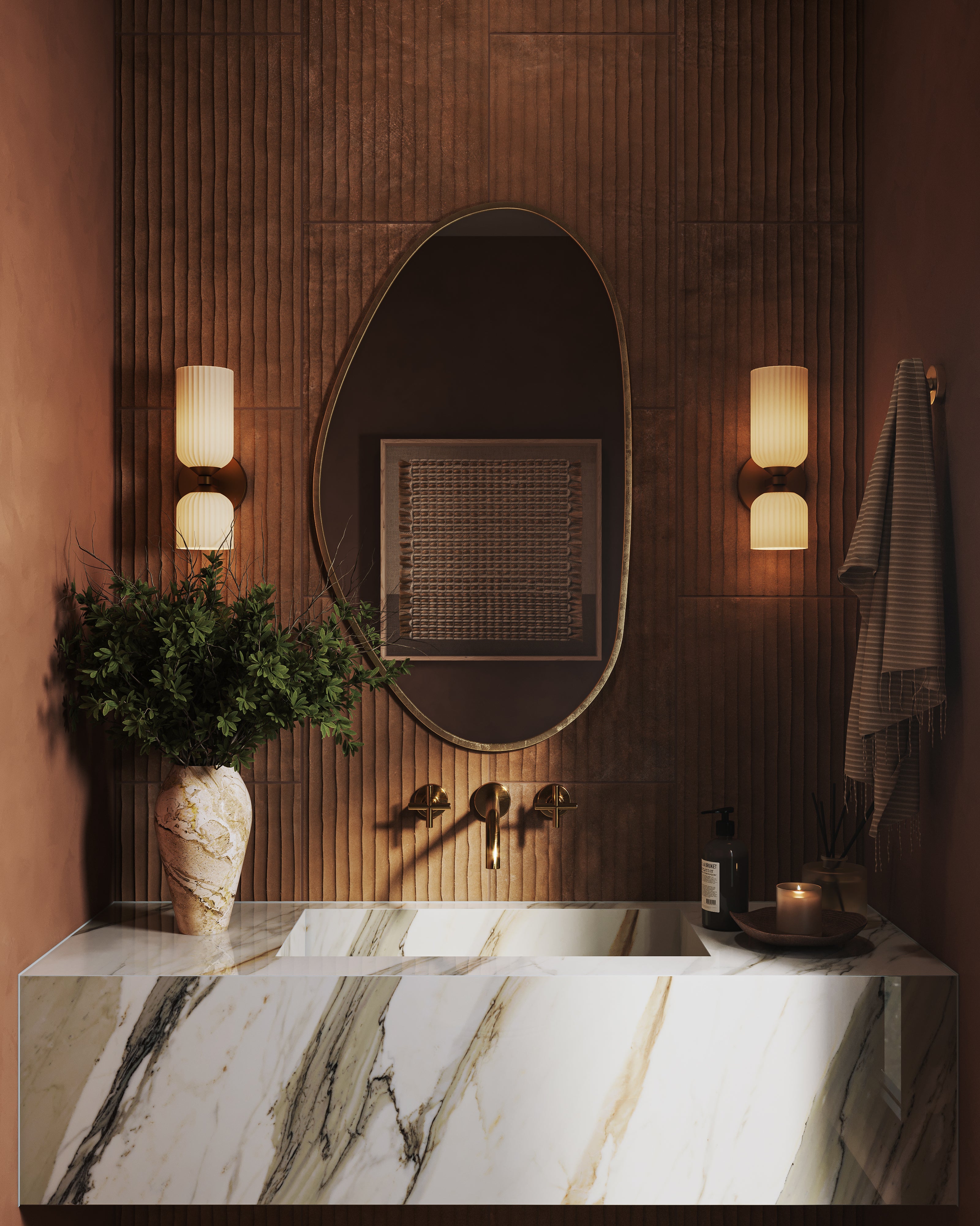 Moody modern bathroom vanity with a marble countertop and integrated sink, featuring an oval brass-framed mirror, ribbed terracotta wall tiles, warm brass wall sconces, and soft ambient lighting for a refined spa-like feel.