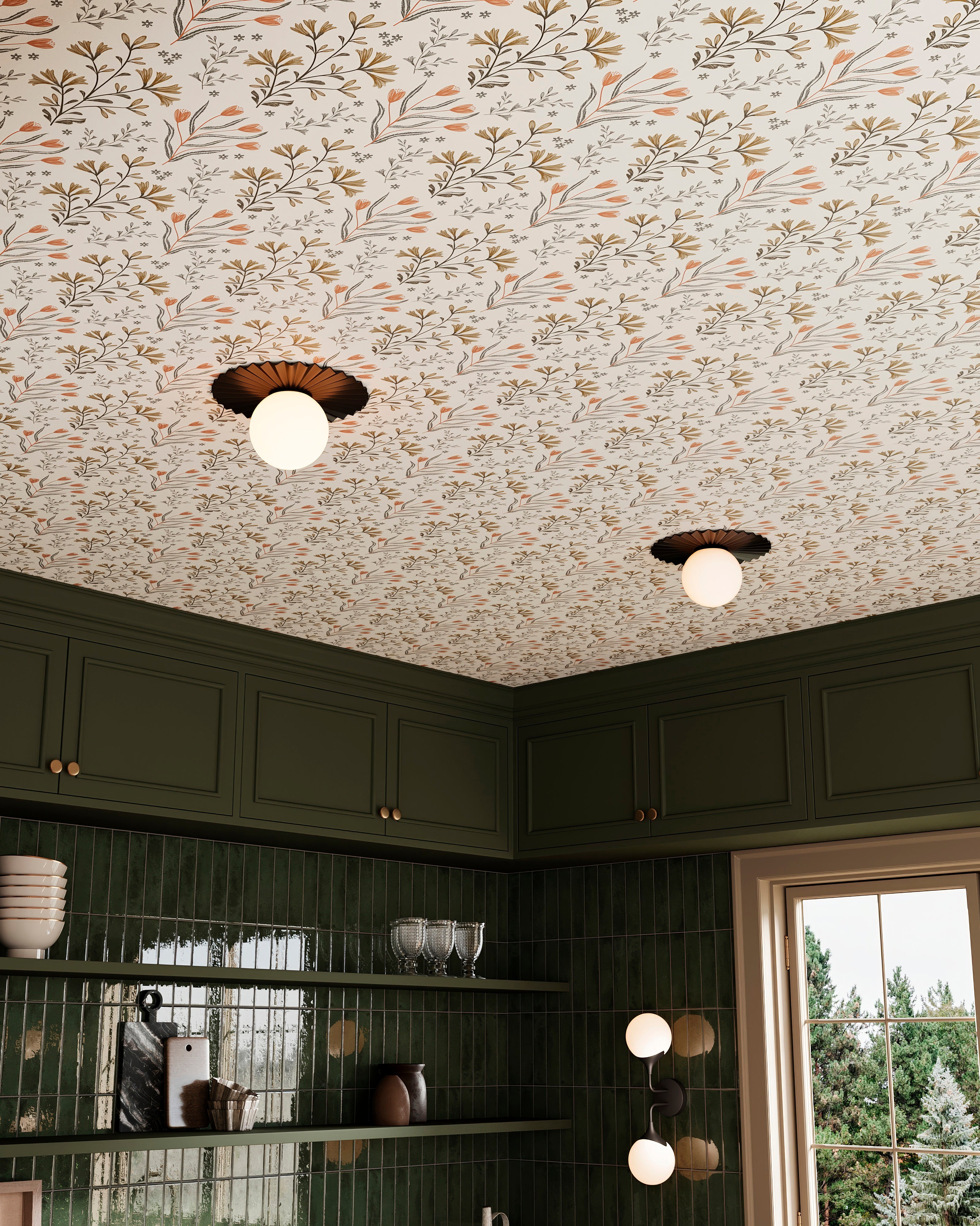 Flush mount ceiling lights with pleated black metal shades and glowing globes set against botanical wallpaper above dark green kitchen cabinetry.