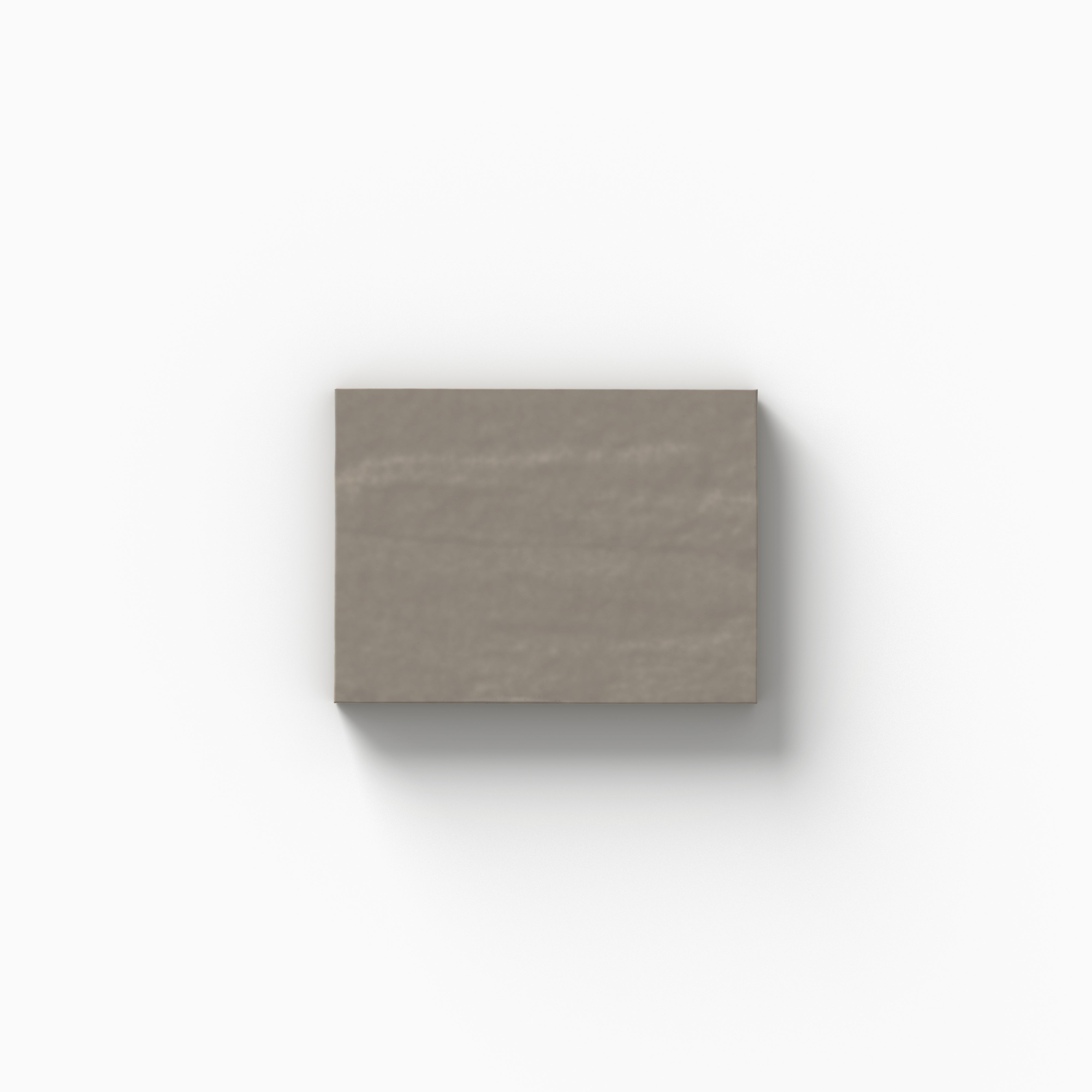 An earthy gray 3x4 porcelain tile sample with a glossy finish, showcasing gentle color movement and handcrafted character on a white backdrop.