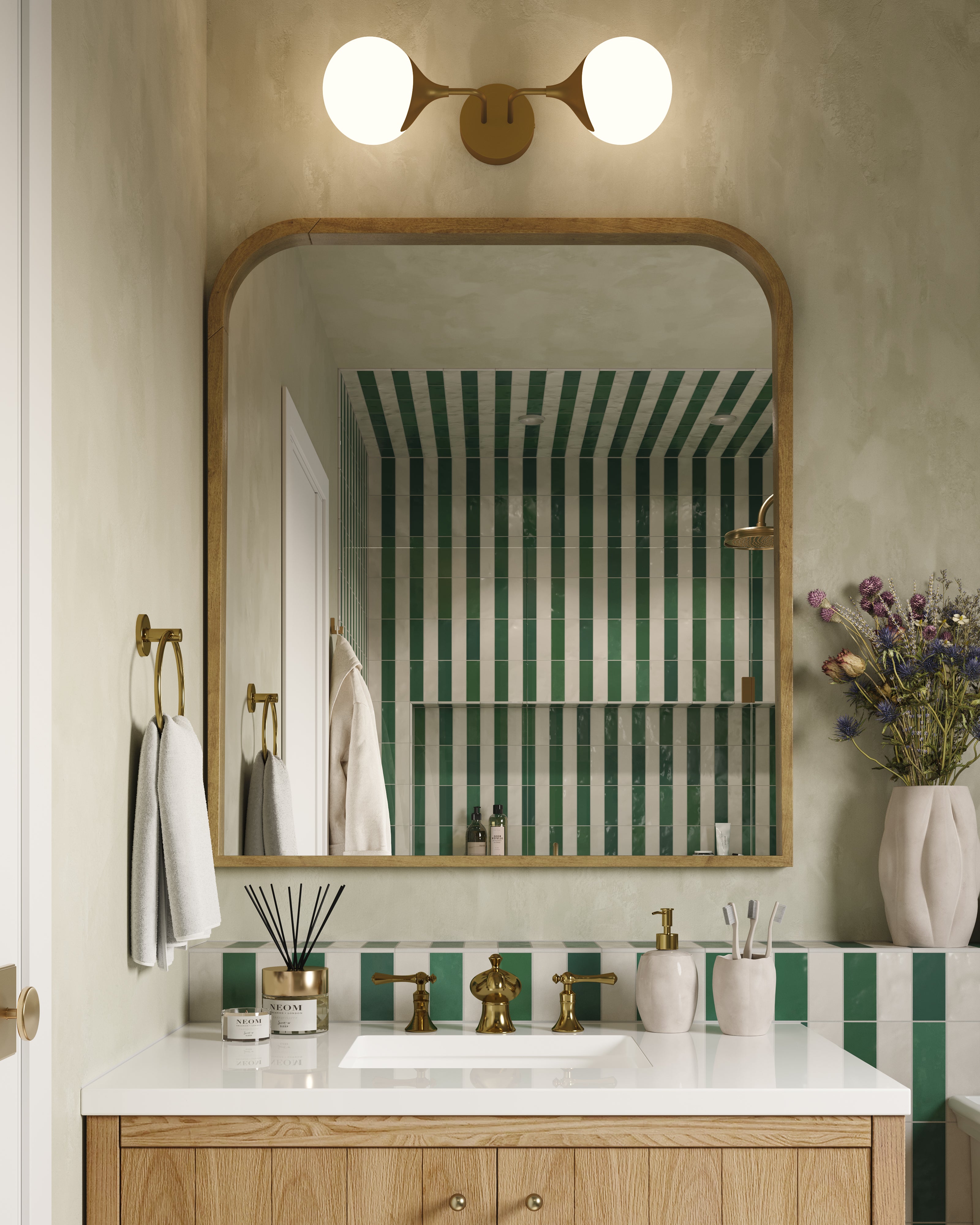 Brushed gold globe vanity light mounted above an arched mirror, casting warm light over a bathroom sink with green striped tiles and brass accents.