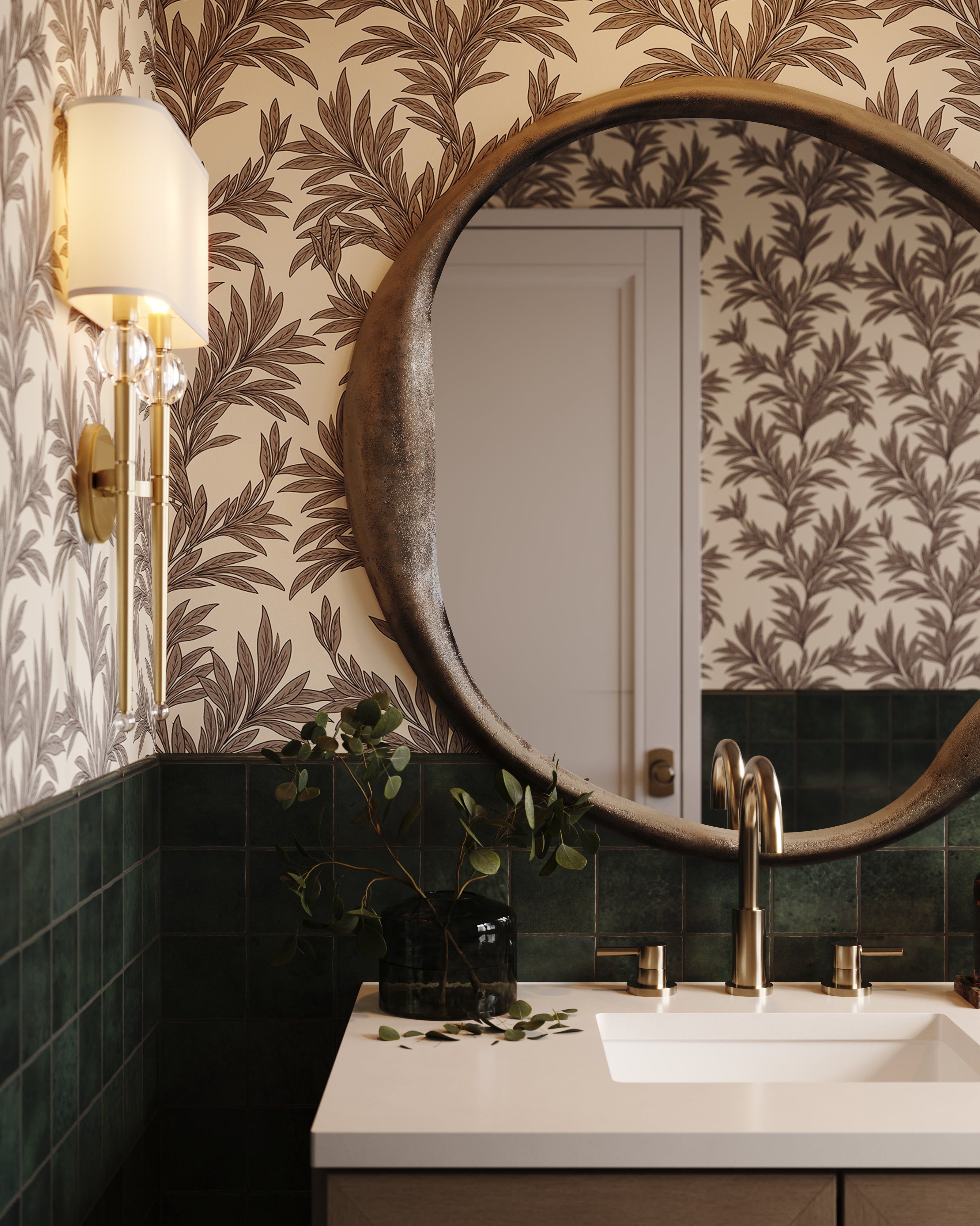 Botanical wallpaper and black wall tile surround a round mirror above a bathroom vanity, accented by brass fixtures and leafy greenery.