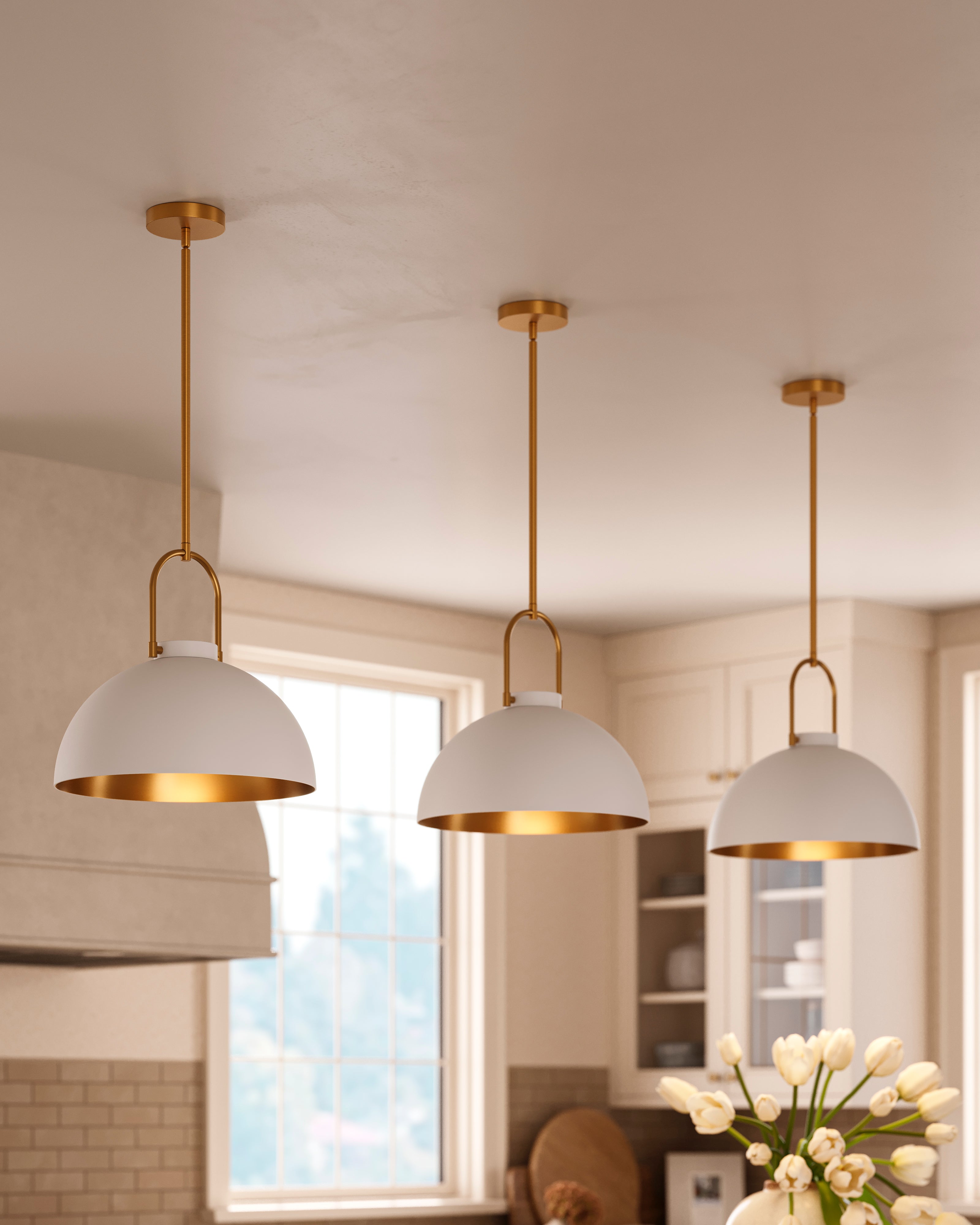 Three white dome pendant lights with gold interiors and brushed gold suspension hanging above a kitchen island.